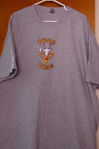 T-shirt avec un chat assis sur une pointe de pizza avec l'écriture « Pizza Time» au-dessus et en en dessous.